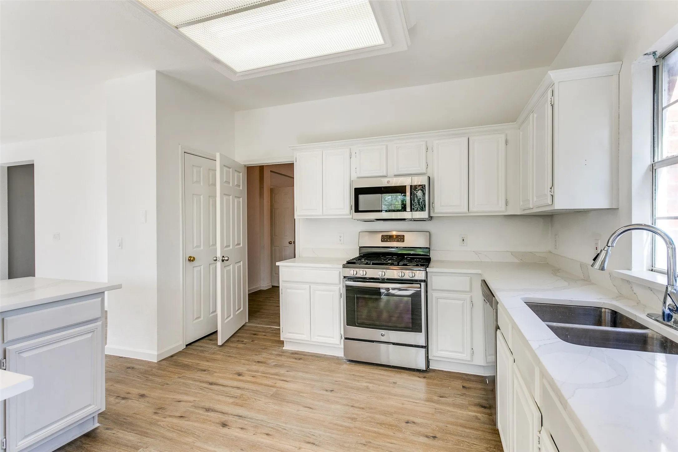 Kitchen with sink, light hardwood / wood-style flooring, white cabinets, and stainless steel appliances