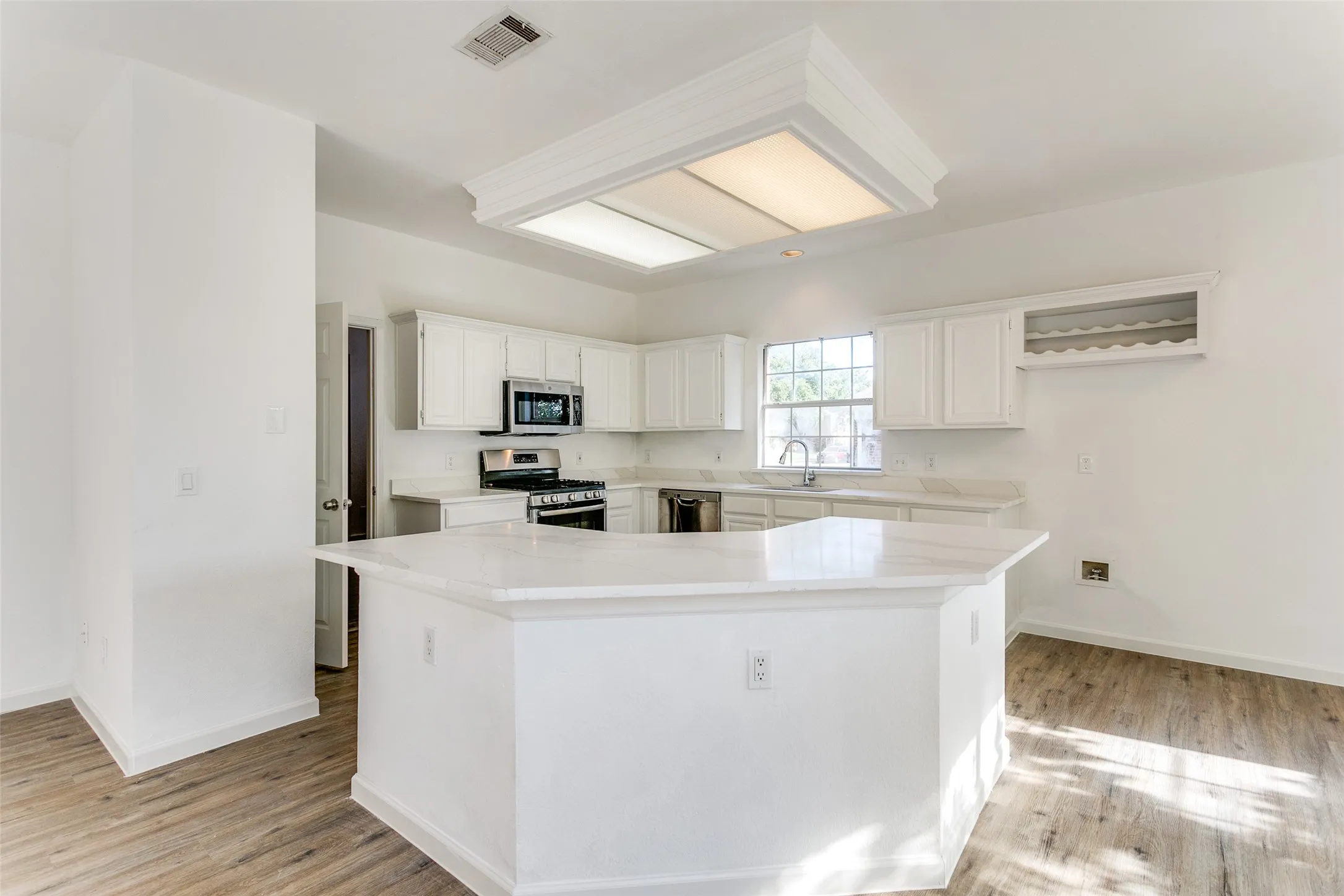 Kitchen with light hardwood / wood-style flooring, white cabinets, a center island, appliances with stainless steel finishes, and sink