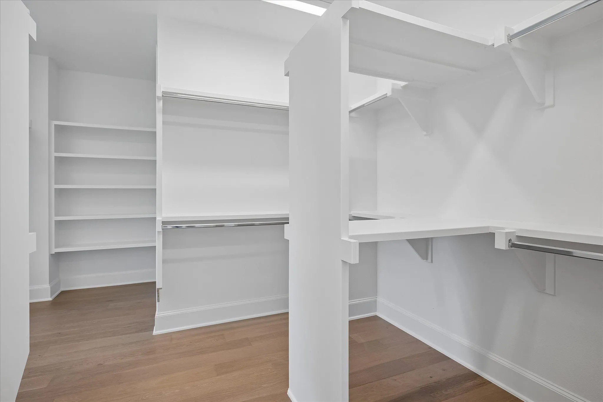 Spacious walk-in closet featuring multiple shelving units, dual hanging rods at varying heights, and wood-finish flooring throughout