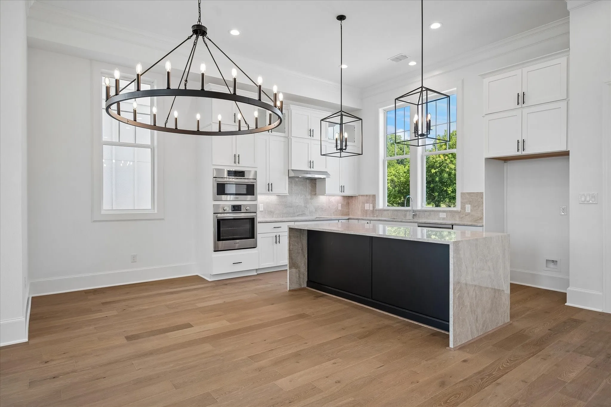 Chef's kitchen featuring a large waterfall-edge island with wood-finish base, white cabinetry with hardware accents, stainless steel built-in appliances, quartz countertops, and pendant lighting