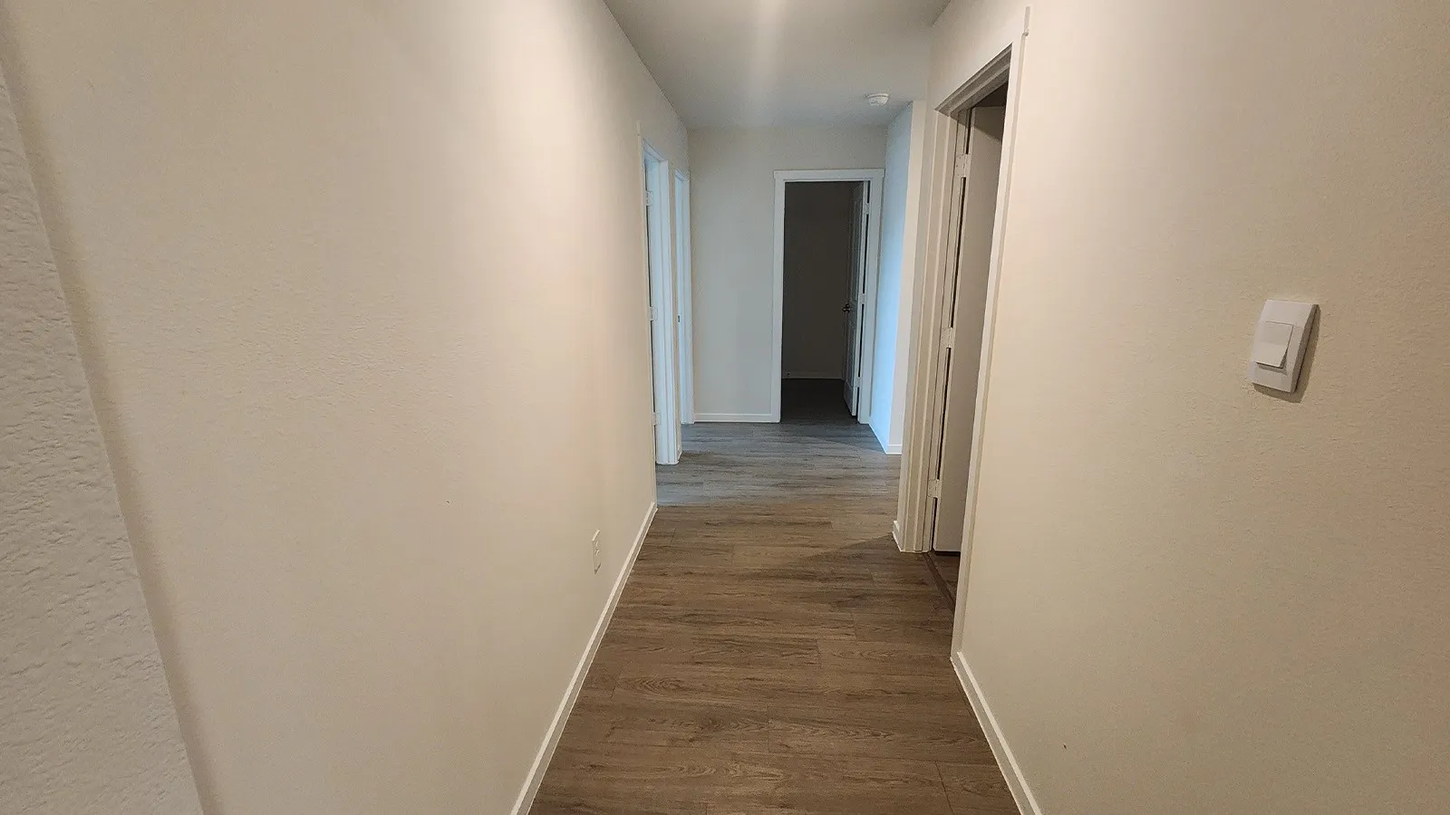 A well-lit hallway featuring wood-finish flooring, neutral wall tones, and white trim