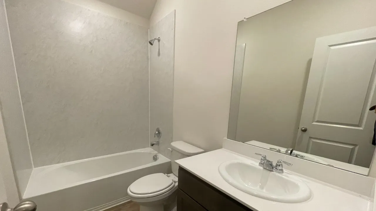 Contemporary bathroom featuring a white tub with a textured shower surround, a sleek white vanity countertop, an integrated oval sink, and chrome fixtures