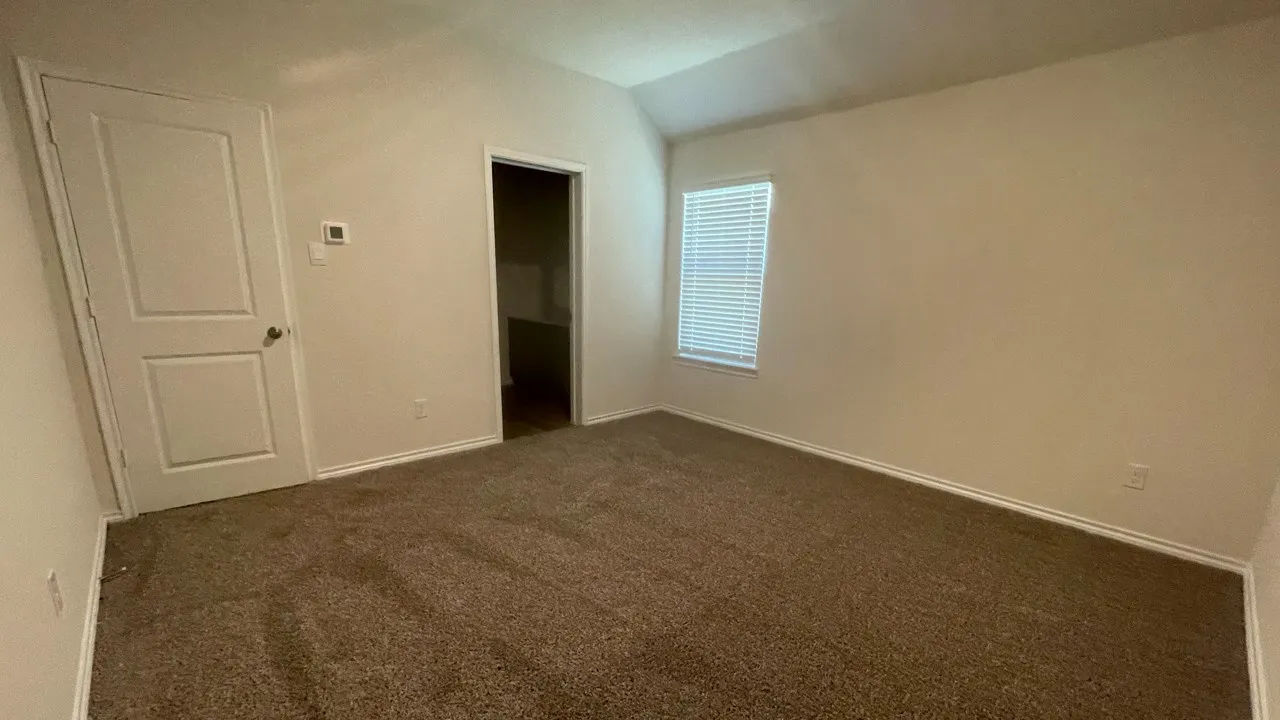 Carpeted room featuring a single window with blinds, a vaulted ceiling, and a white interior door