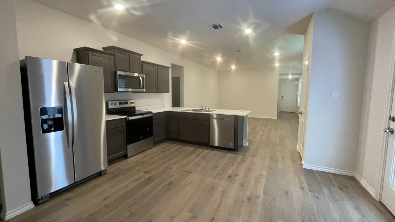 Contemporary kitchen featuring stainless steel appliances, dark wood-finish cabinetry, a large kitchen island with a sink, recessed lighting, and wood-finish flooring