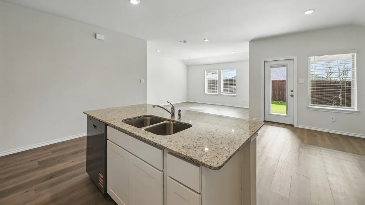 Open-concept kitchen featuring a spacious island with a double basin sink, light-toned granite countertop, and integrated dishwasher