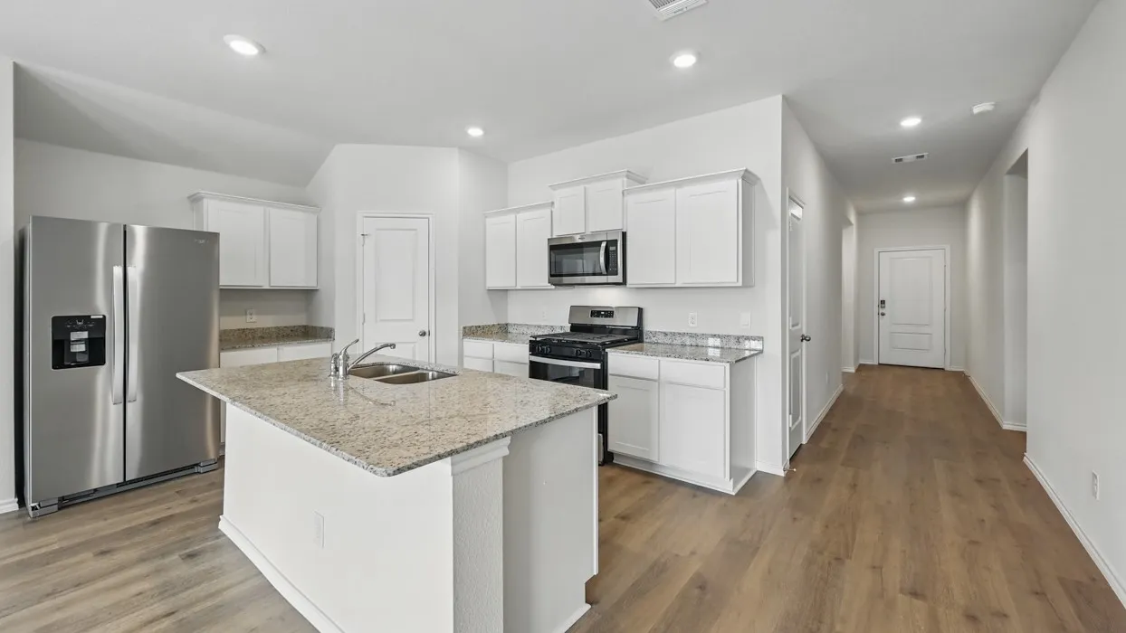 Modern kitchen featuring white cabinetry, a central island with a double basin sink, stainless steel appliances, and light-toned granite countertops