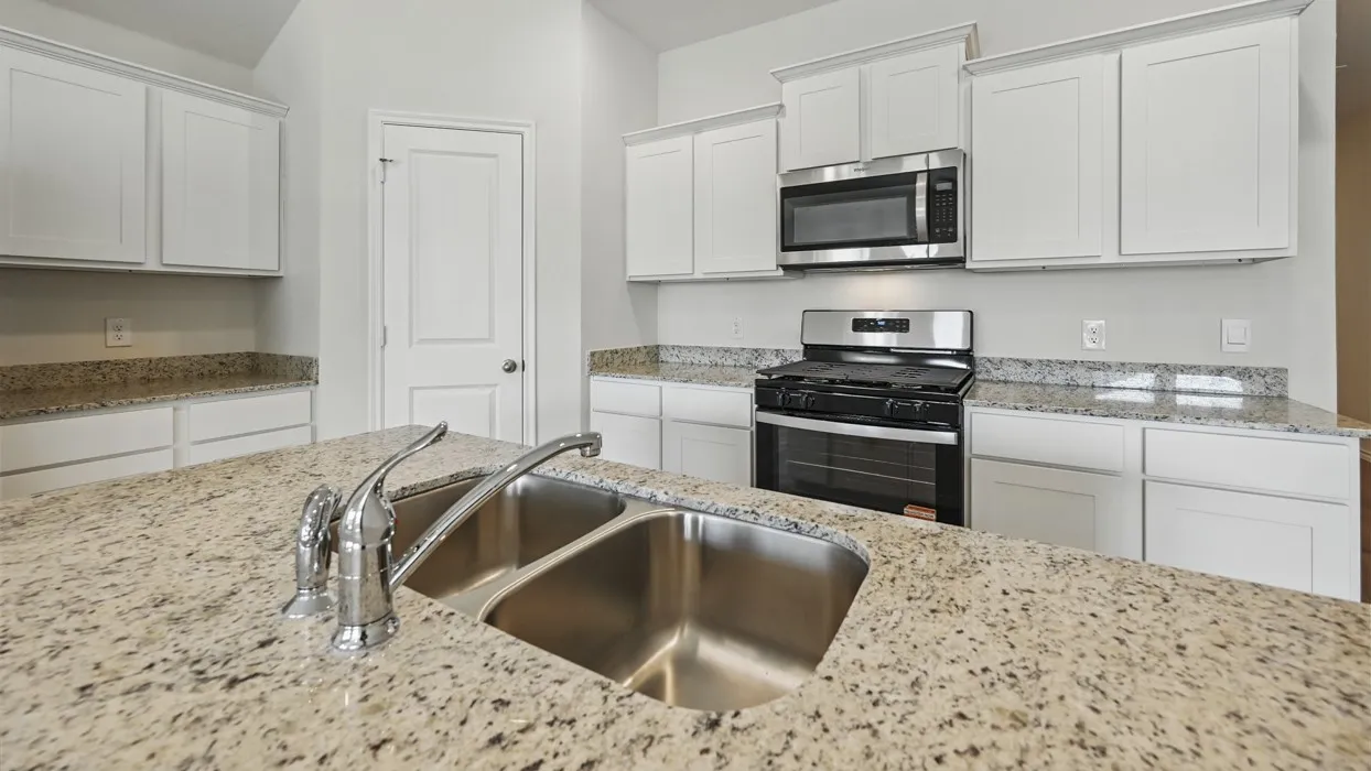Kitchen island featuring a double basin stainless steel sink with a chrome pull-down faucet, surrounded by light-toned granite countertops