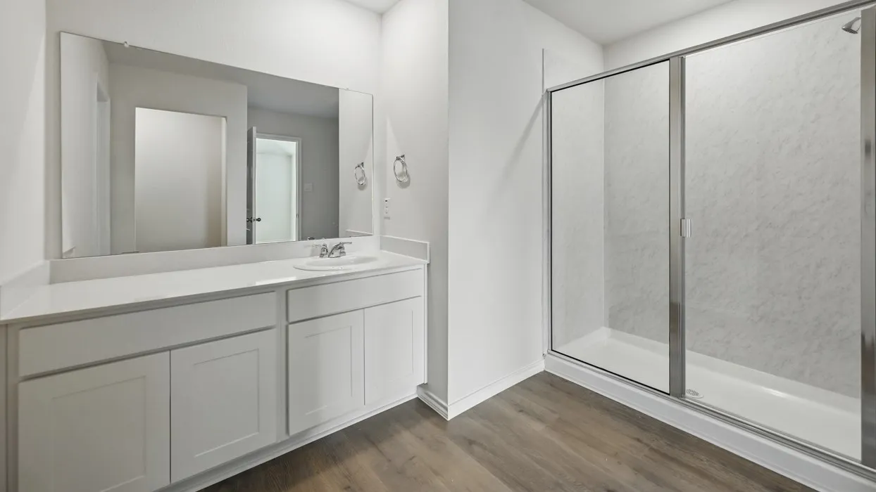 Bathroom featuring a white vanity with integrated sink, a large wall-mounted mirror, a glass-enclosed shower with sliding doors, and wood-finish flooring