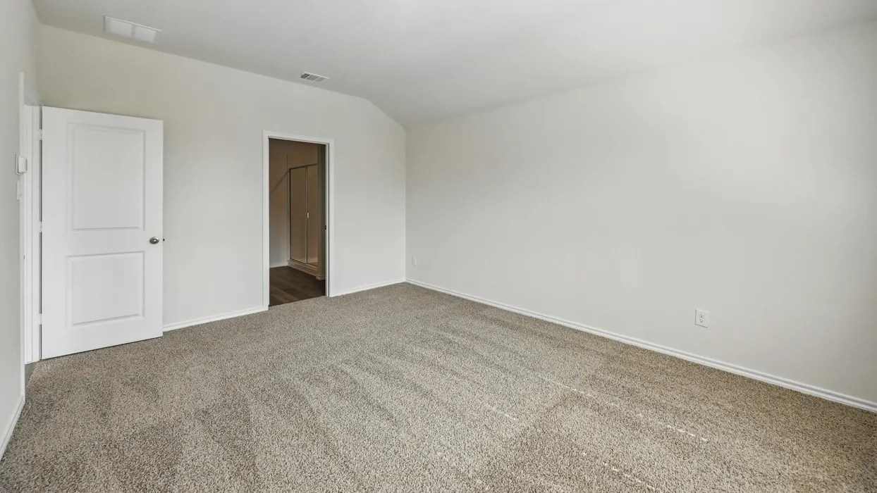 Spacious carpeted room featuring a white interior door, light-toned walls, and a vaulted ceiling