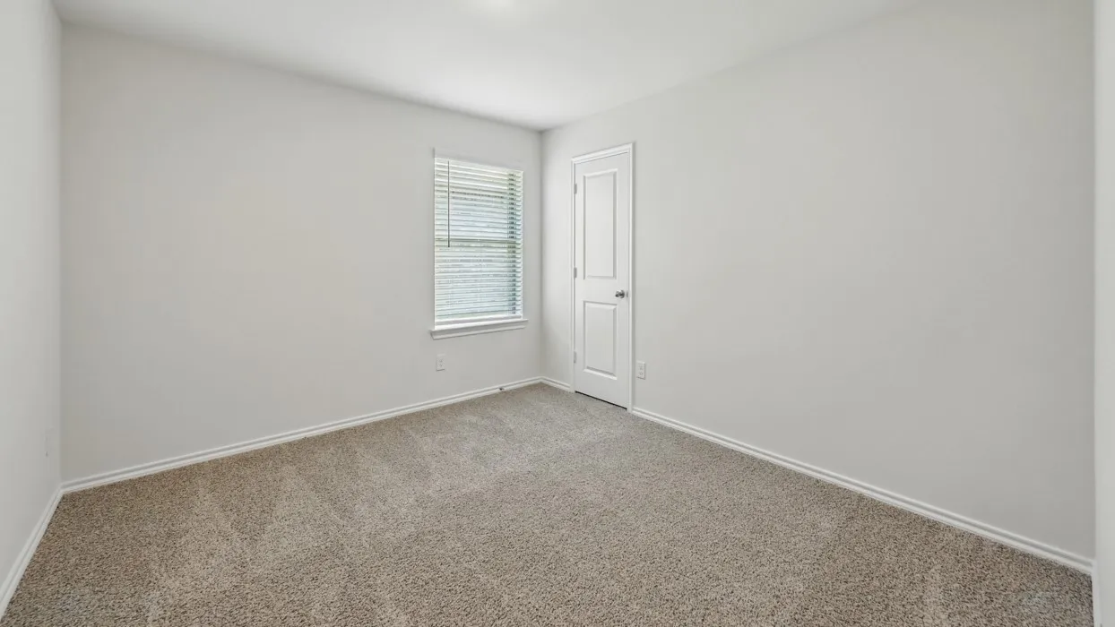 Neutral-toned carpeting extends throughout this room, featuring a single window with horizontal blinds and a white paneled door