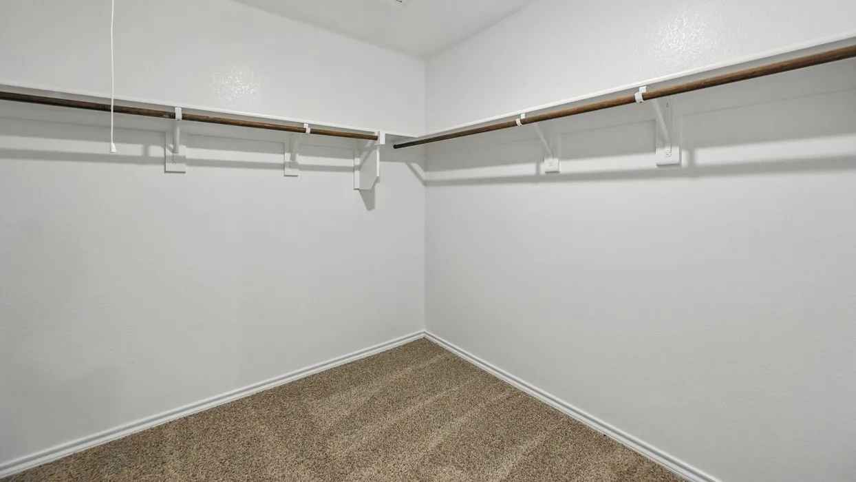 Spacious closet featuring abundant hanging storage, neutral carpet flooring, and white baseboards