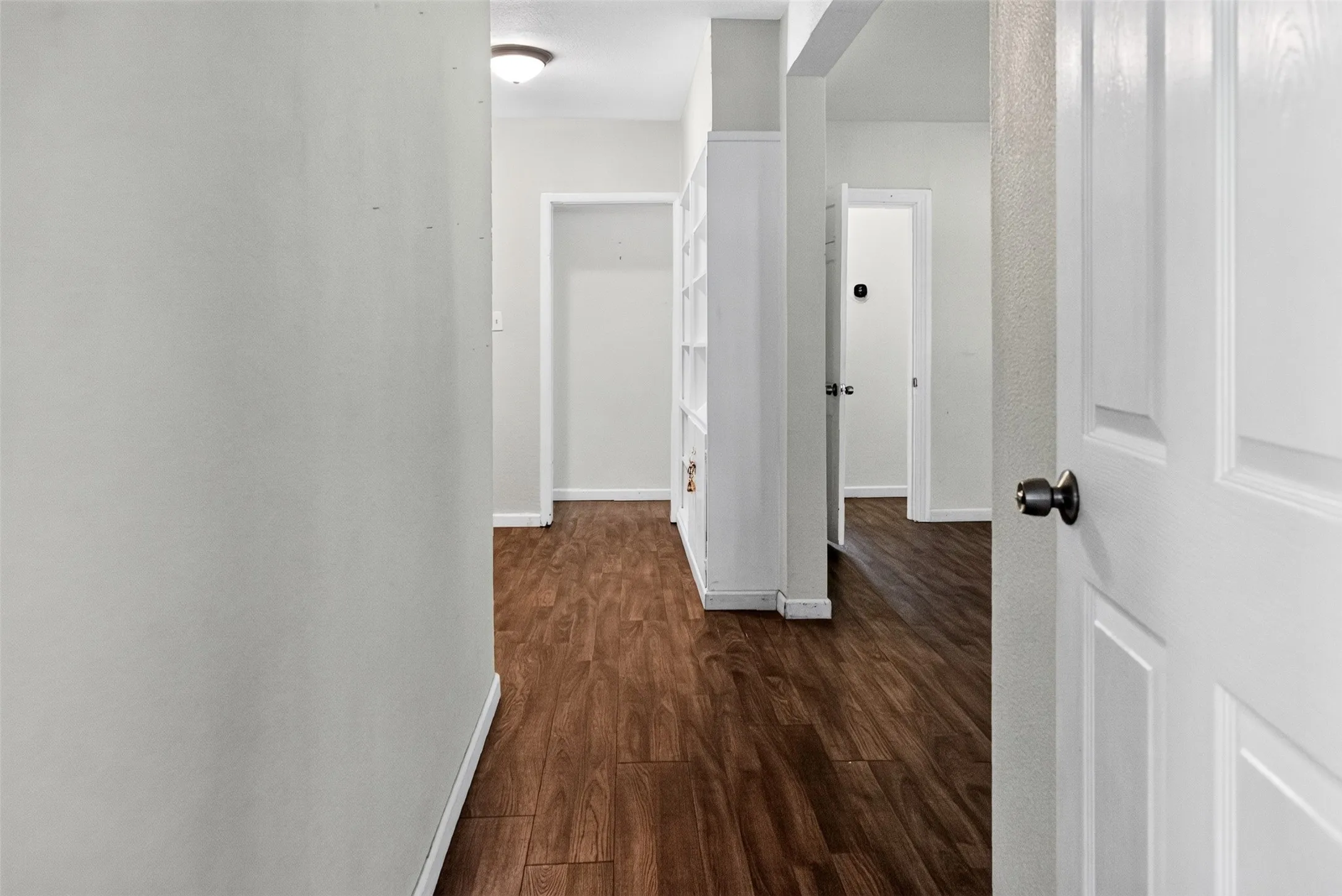 Hallway featuring wood-finish flooring, white walls, and a built-in shelving unit