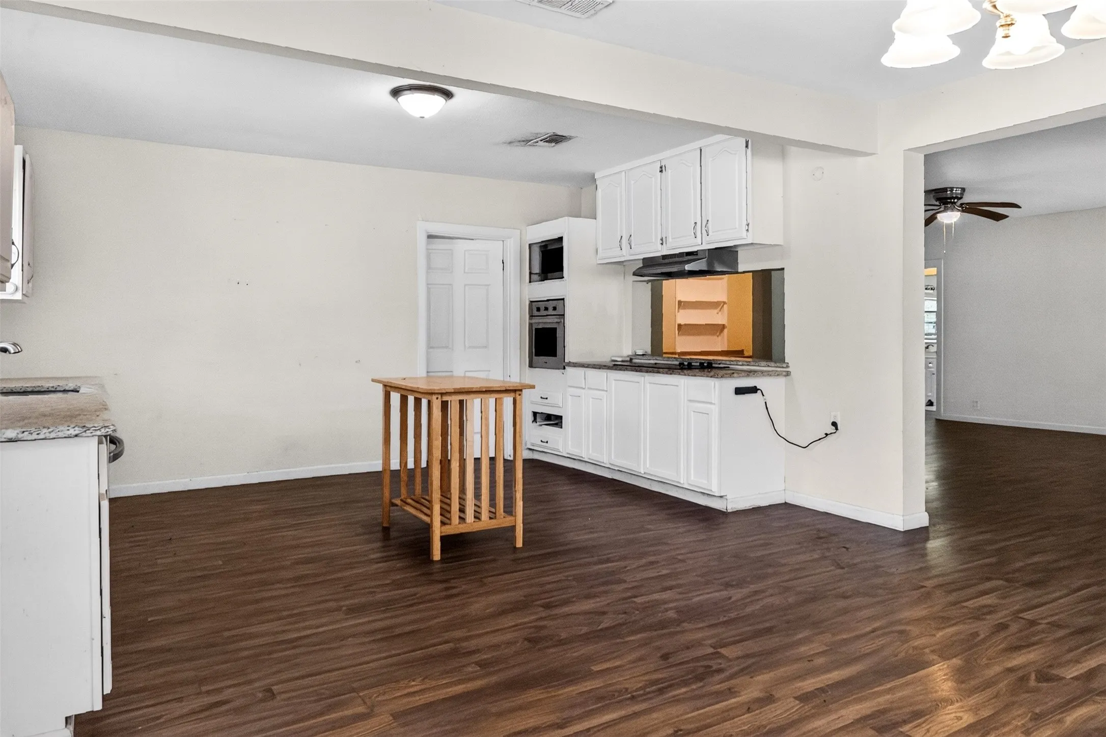 Open-concept kitchen with wood-finish flooring, white cabinetry, integrated wall oven, and built-in microwave