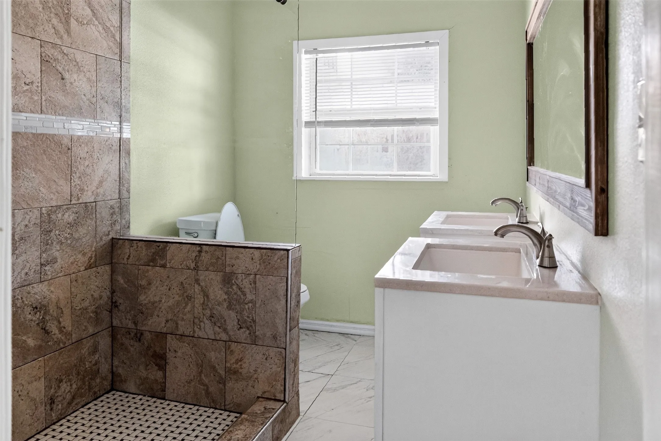 Bathroom featuring a tiled walk-in shower with mosaic floor, dual vanity with undermount sinks, and a framed mirror