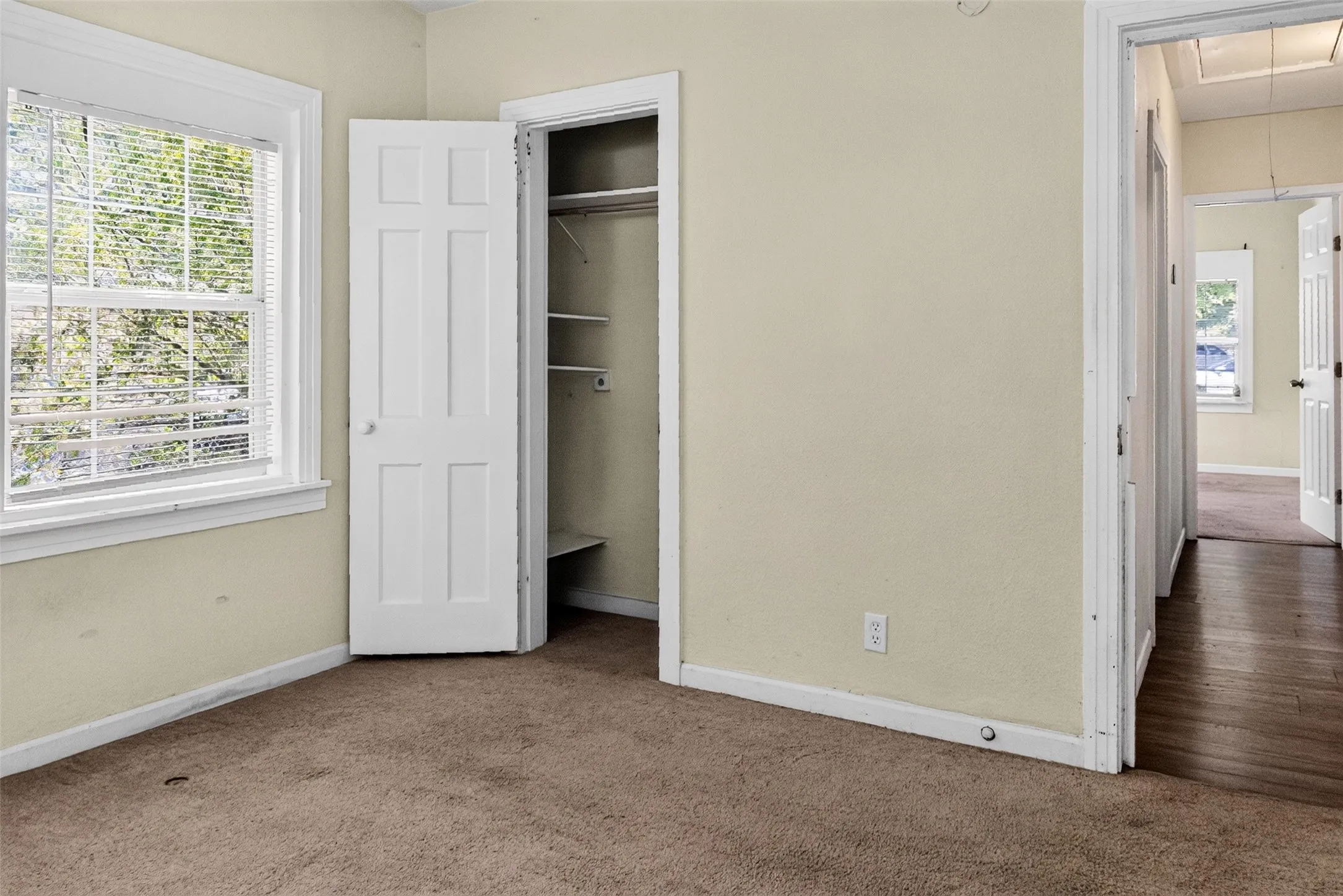 Carpeted room featuring a white-trimmed window, a six-panel interior door, and a built-in closet with shelving and hanging rod