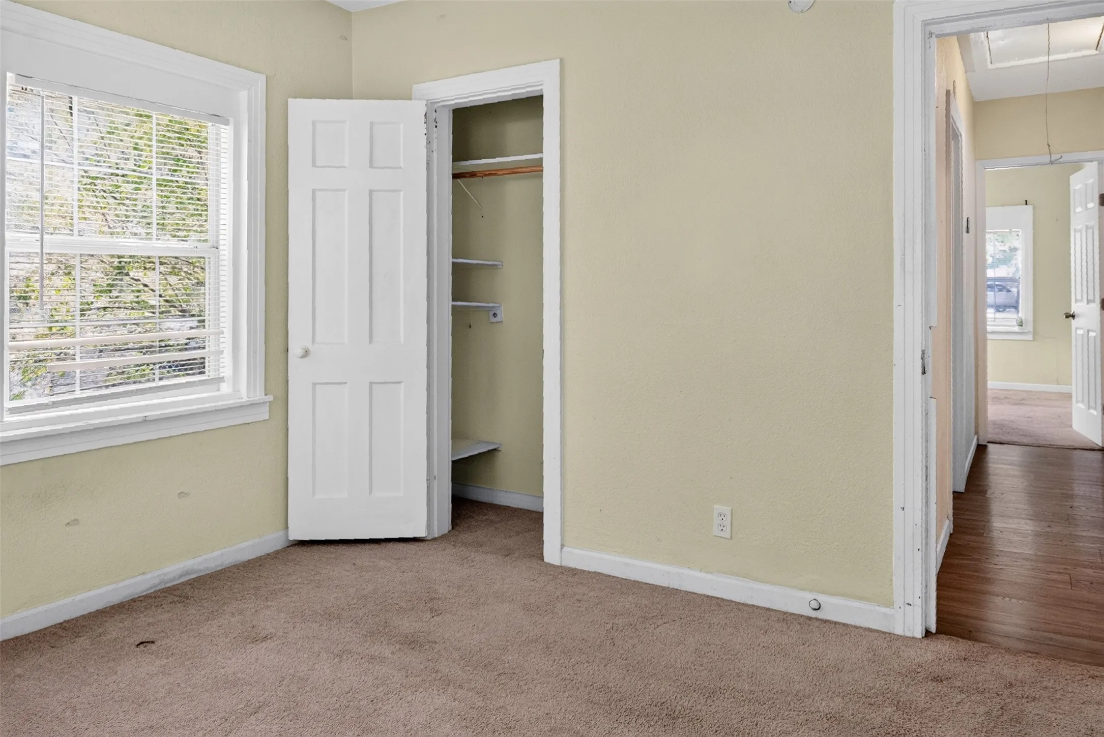 Carpeted room featuring a window with blinds, a paneled door, and built-in closet shelving