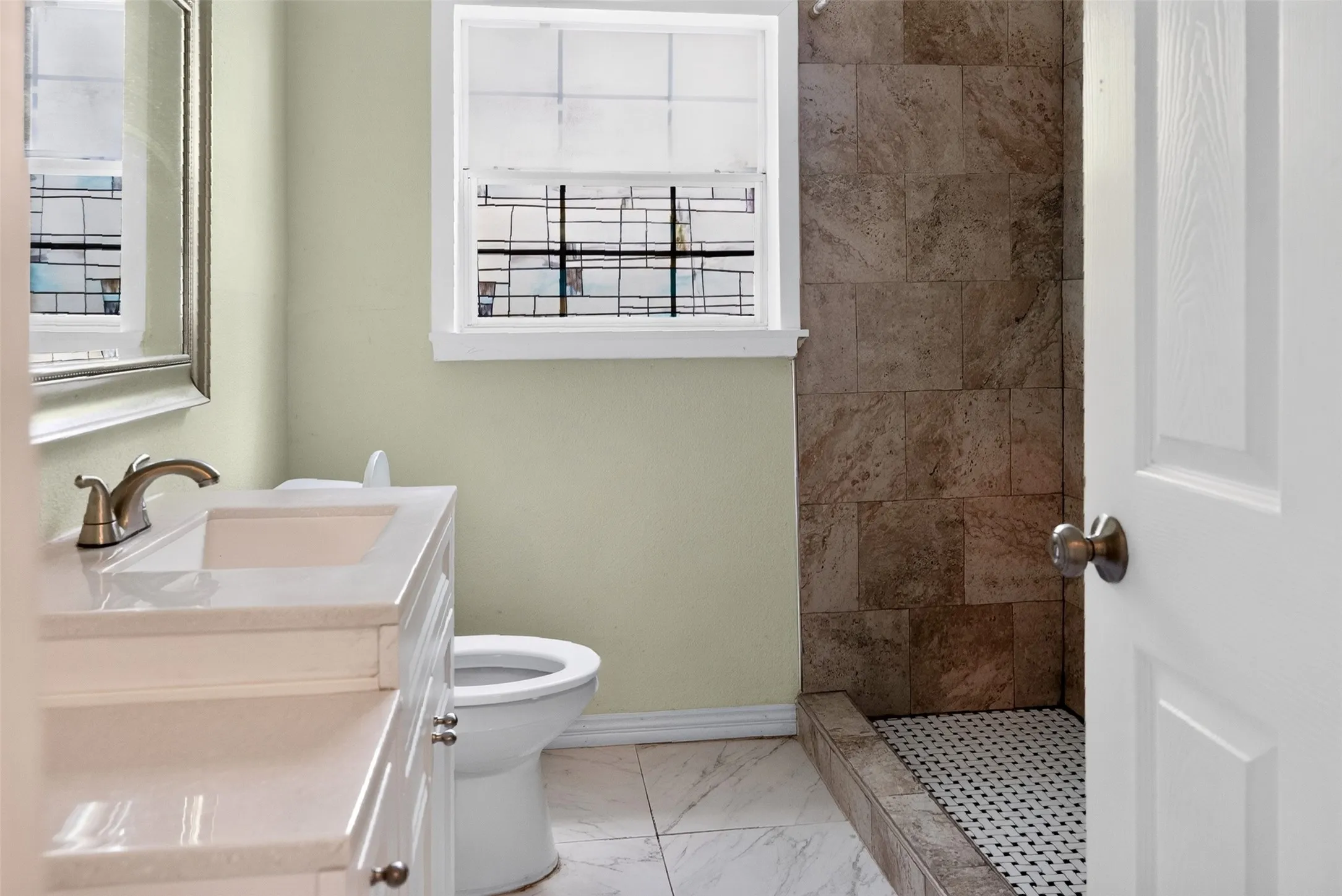 Bathroom featuring a white vanity with an integrated sink, brushed nickel faucet, and framed mirror