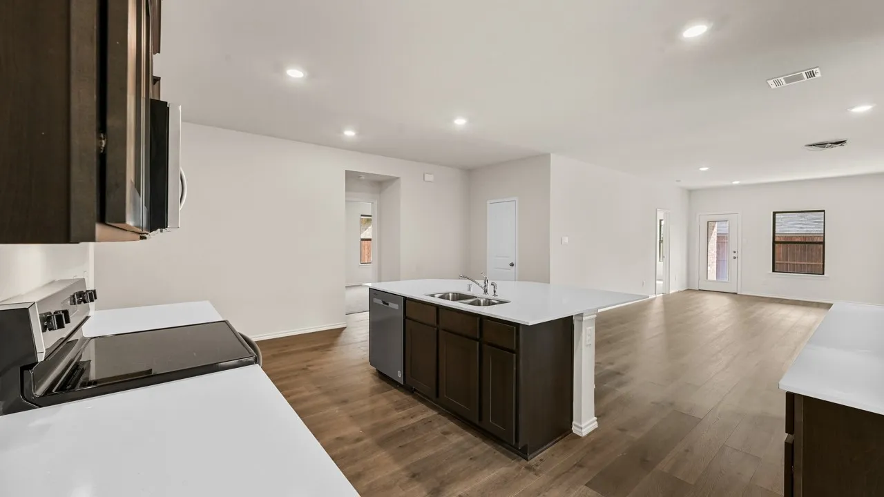 Open-concept kitchen and living area featuring wood-finish flooring, a kitchen island with dual sinks, white countertops, and dark wood cabinetry