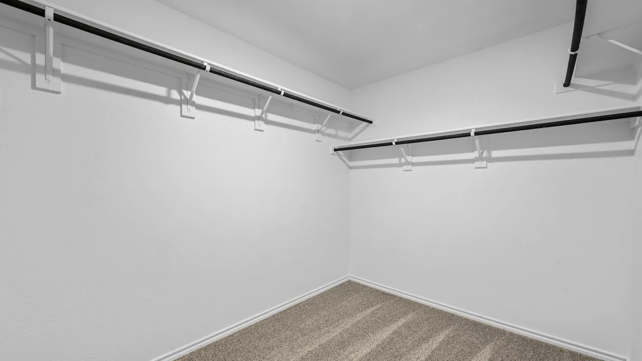 Walk-in closet with textured white walls, light-colored carpet flooring, and white baseboards