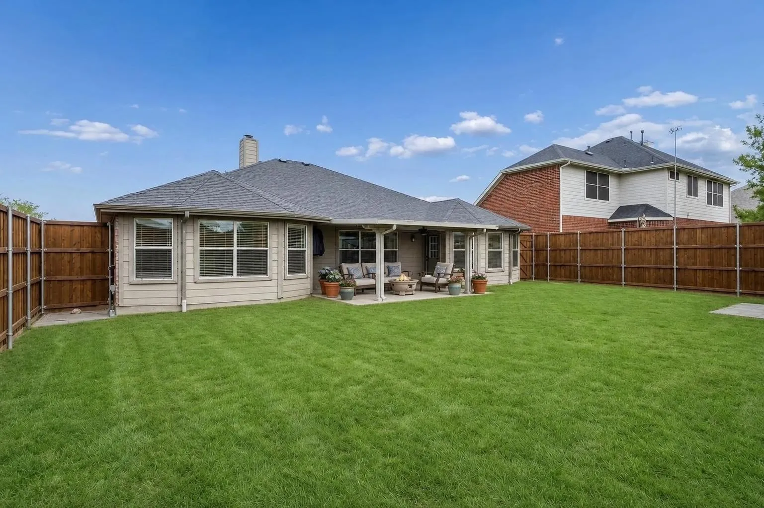 Spacious fenced backyard with covered patio, green lawn, privacy fencing, and room for outdoor living, play, pets, or entertaining.