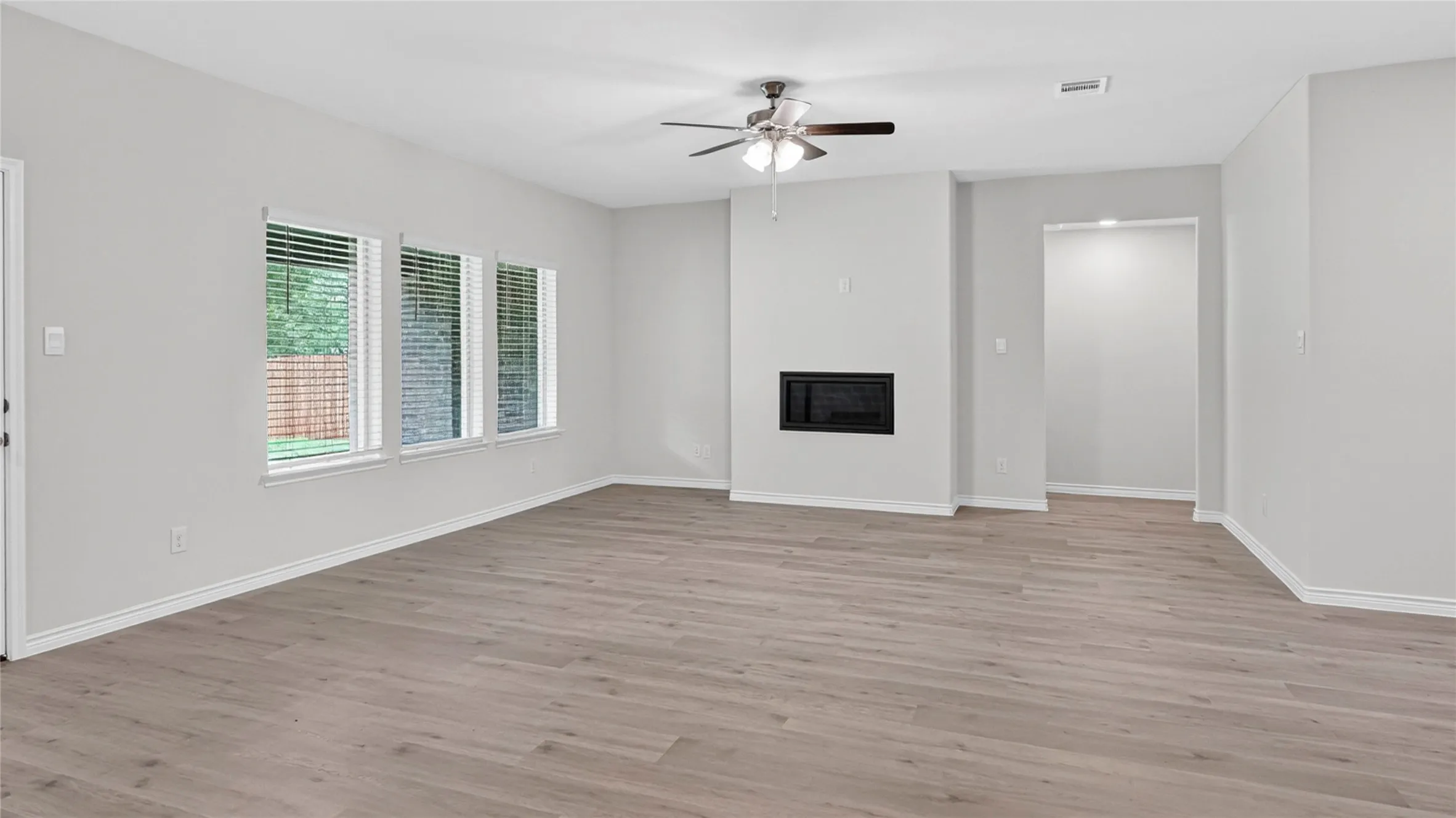 Open-concept living area featuring light wood-finish flooring, a contemporary fireplace, and a ceiling fan with integrated​​‌​​​​‌​​‌‌​‌‌​​​‌‌​‌​‌​‌​​​‌​​ lighting