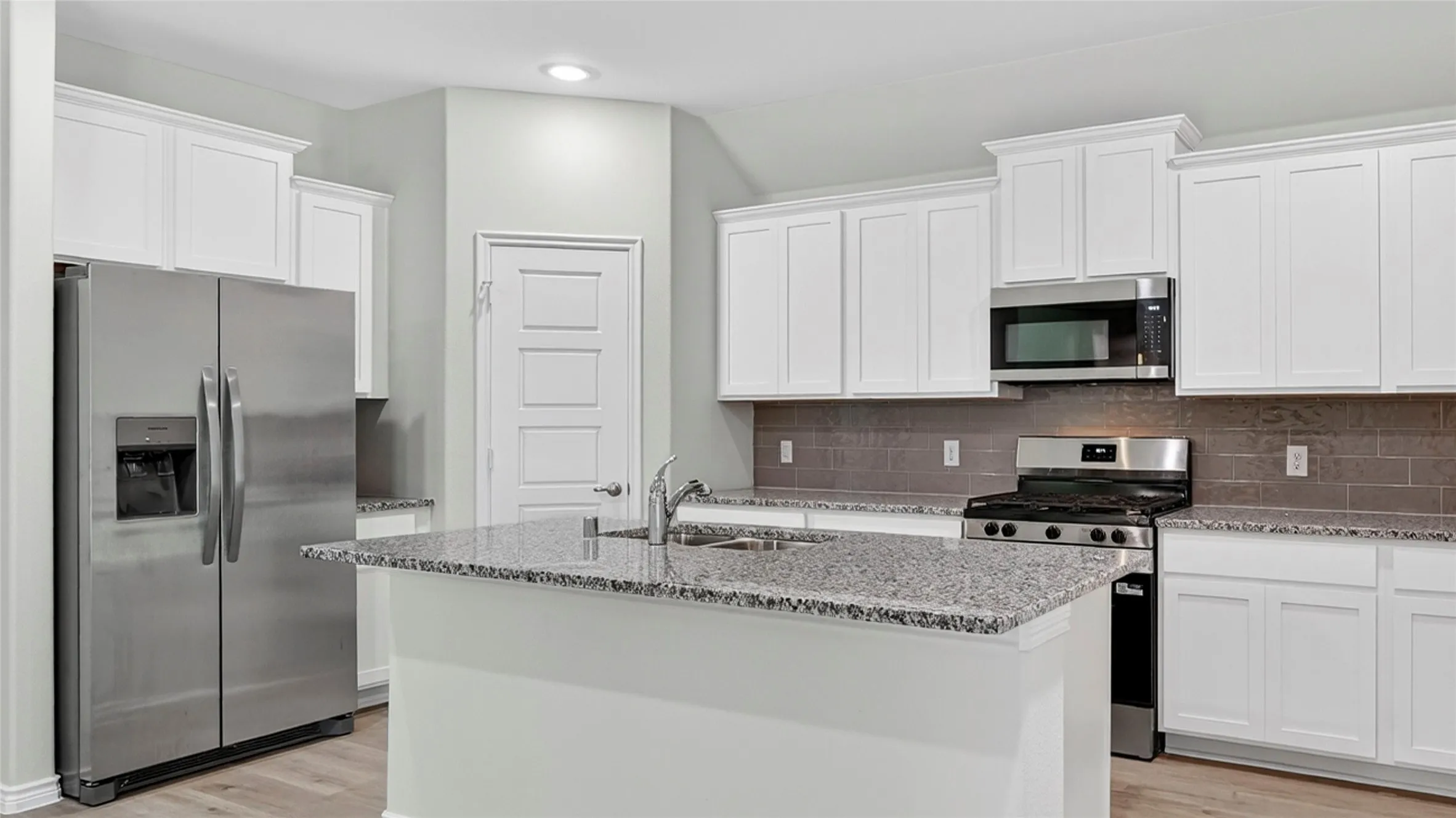 Contemporary kitchen featuring an island with a stainless steel sink, white cabinetry, granite countertops, stainless steel appliances, and wood-finish flooring