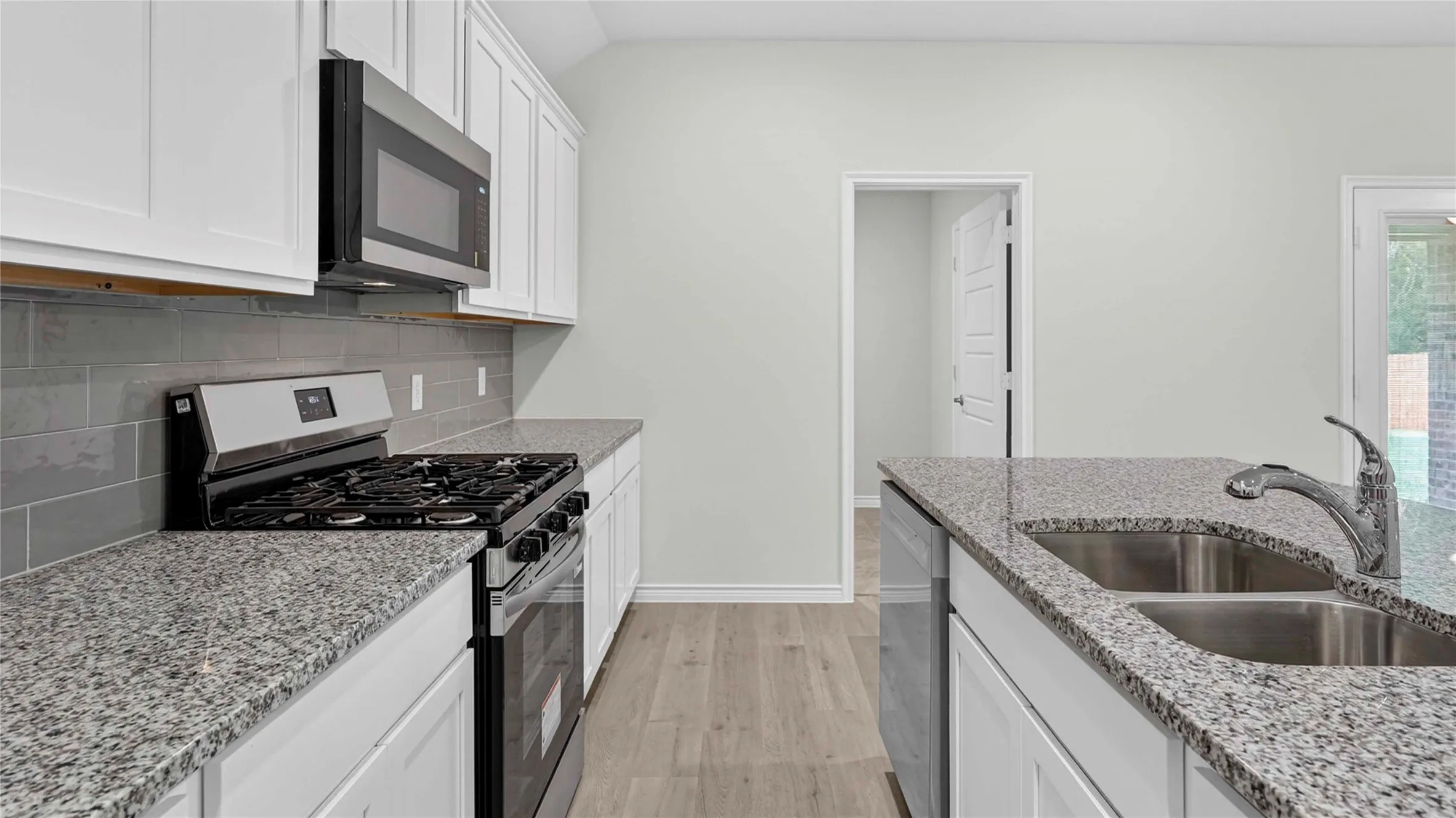 Modern kitchen featuring white cabinetry, granite countertops, a stainless steel gas range, and an undermount double basin sink with a chrome faucet