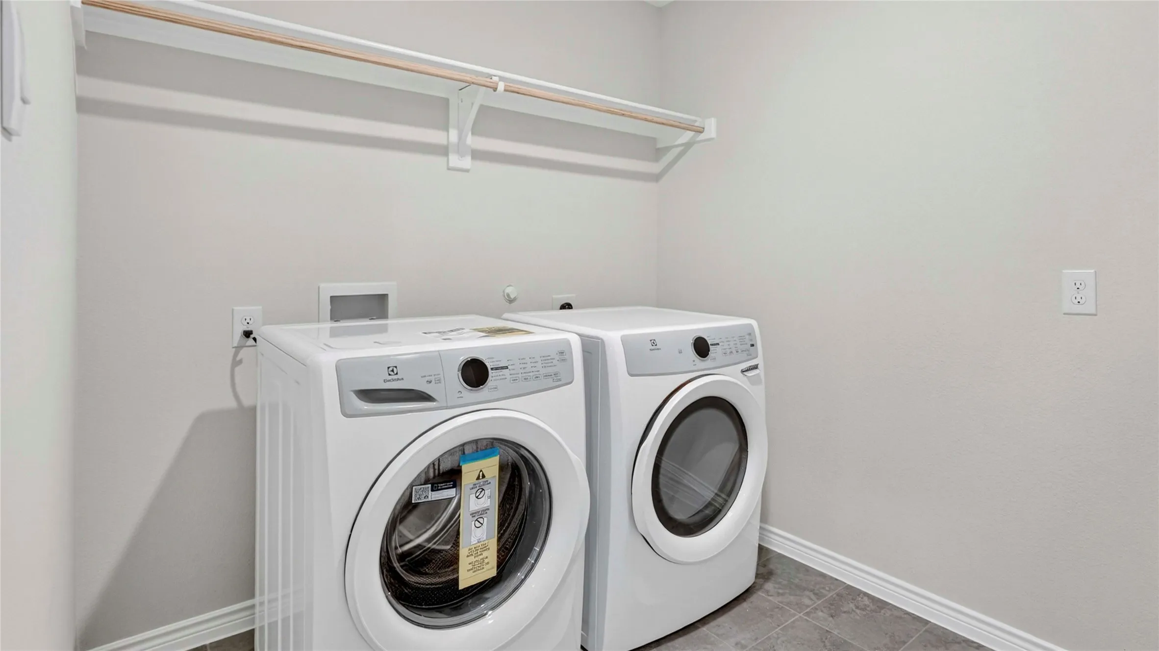 Laundry area featuring light gray wall paint, a built-in hanging rod, and dark gray tile flooring