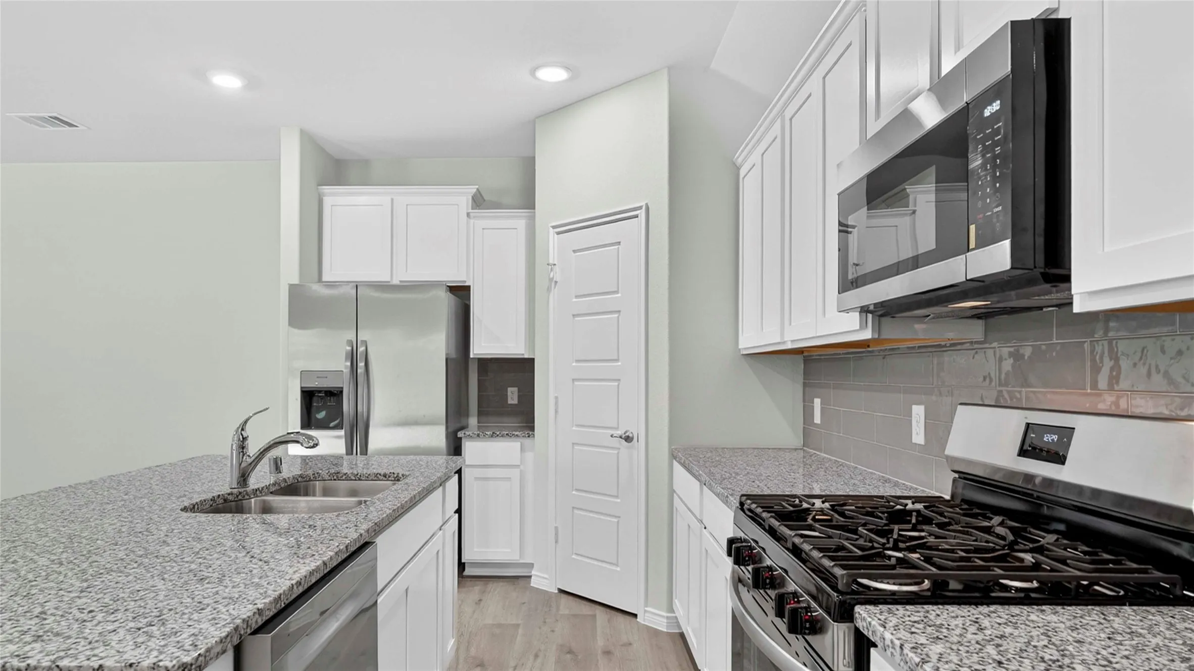 Kitchen featuring granite countertops, stainless steel appliances, a gas range, white cabinetry, and a subway tile backsplash