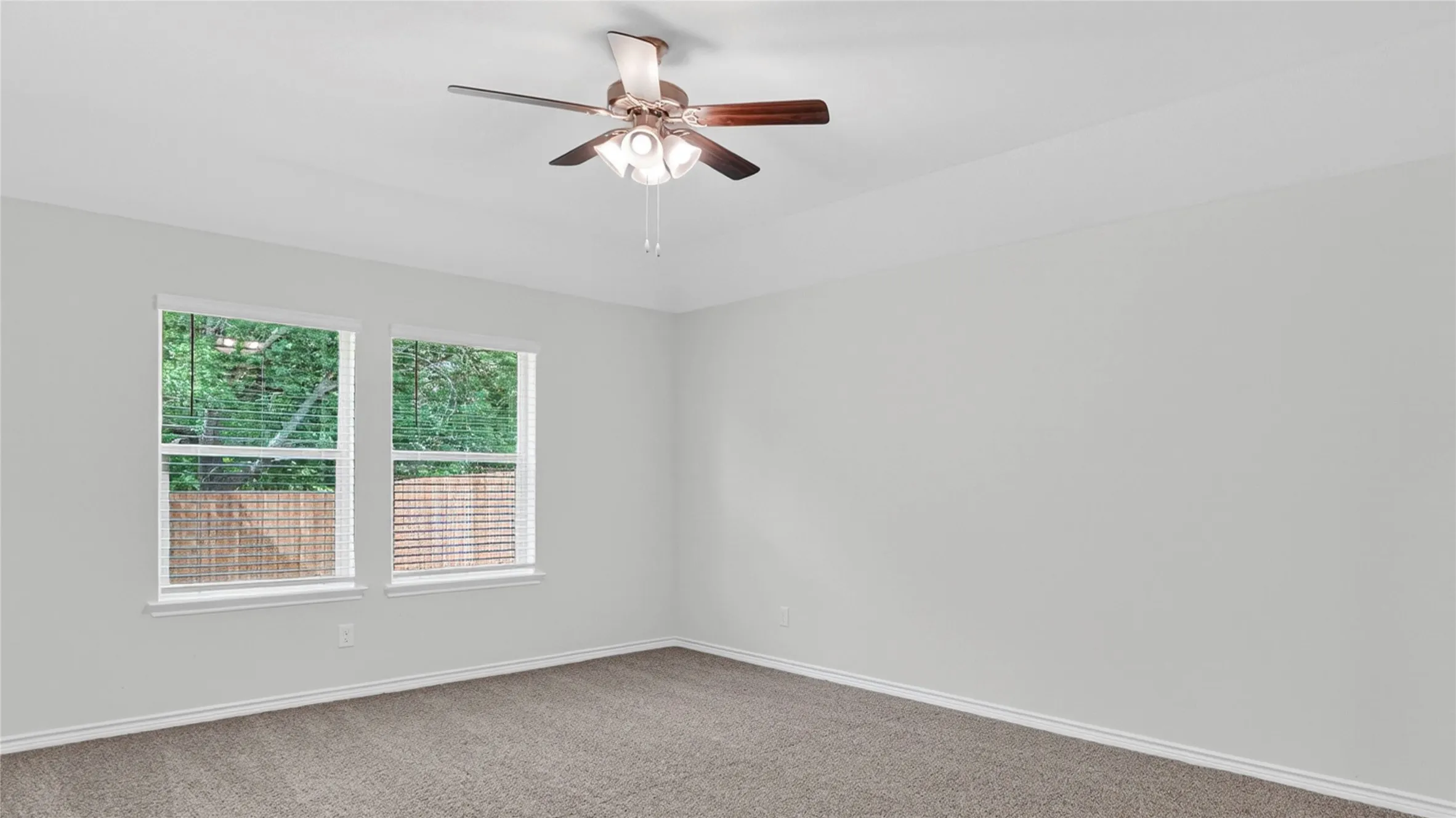 Spacious room featuring neutral paint, plush carpeting, a ceiling fan with integrated lighting, and two windows with blinds