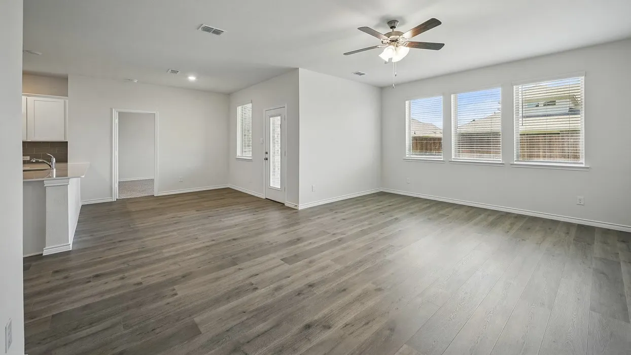 Spacious living area featuring wood-finish flooring, ample natural light from multiple windows, a ceiling fan with integrated lighting, and recessed ceiling lights