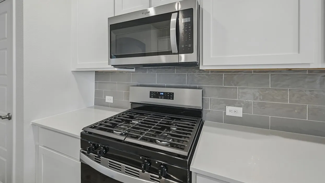 Contemporary kitchen featuring a stainless steel range with a gas cooktop, an over-the-range microwave, white cabinetry, light-toned countertops, and a gray subway tile backsplash