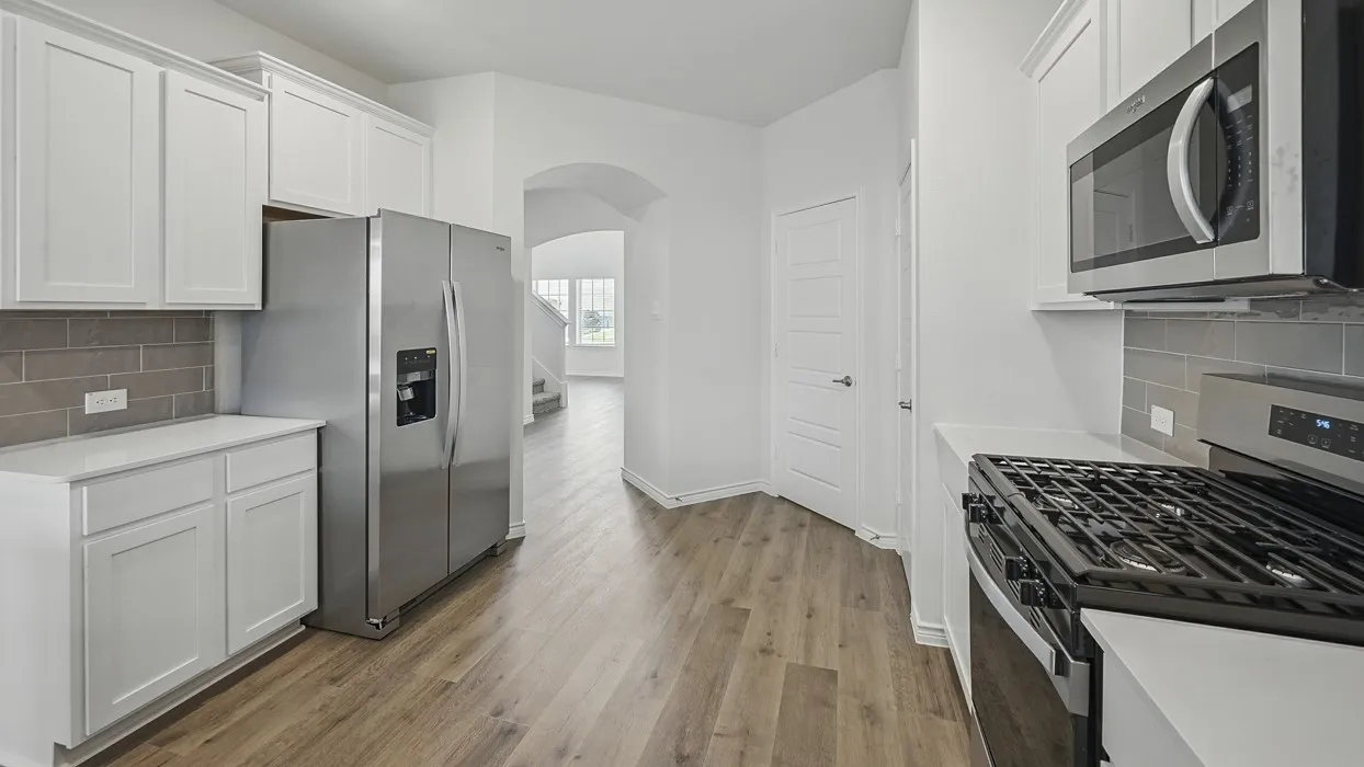 Modern kitchen featuring white cabinetry, gray subway tile backsplash, stainless steel appliances, light-toned wood-finish flooring, and white countertops