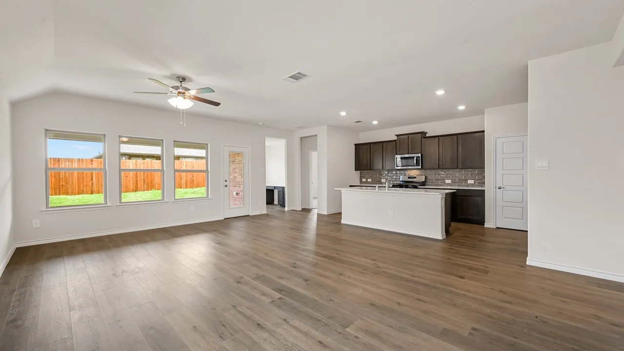 Open-concept living space featuring wood-finish flooring, a contemporary ceiling fan, and multiple windows