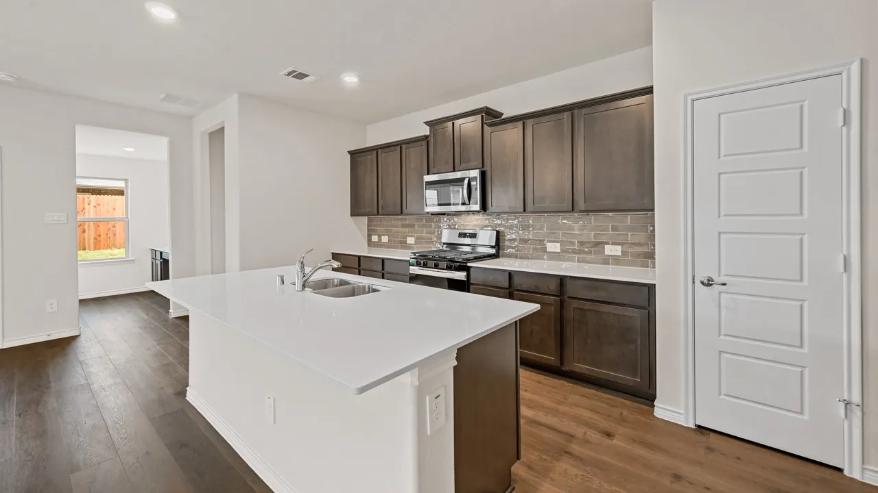 Kitchen featuring a large island with an undermount sink, white countertops, dark wood-finish cabinetry, stainless steel appliances, and wood-finish flooring