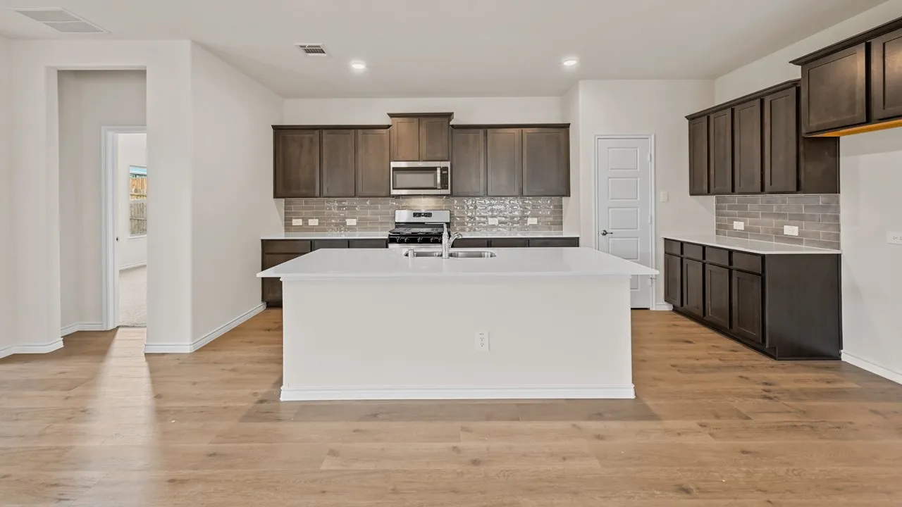 Contemporary kitchen featuring a large central island with a sink, dark wood cabinetry, stainless steel appliances, light gray subway tile backsplash, and light wood-finish flooring