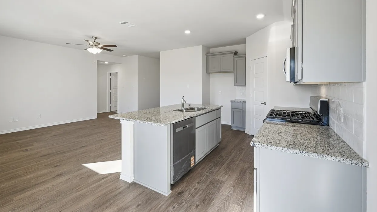 Modern kitchen featuring light gray cabinetry, a gas range, a built-in microwave, and an island with an undermount sink and integrated dishwasher