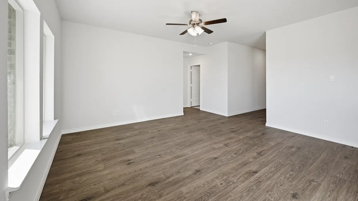 Spacious room featuring wood-finish flooring, white walls, and a ceiling fan