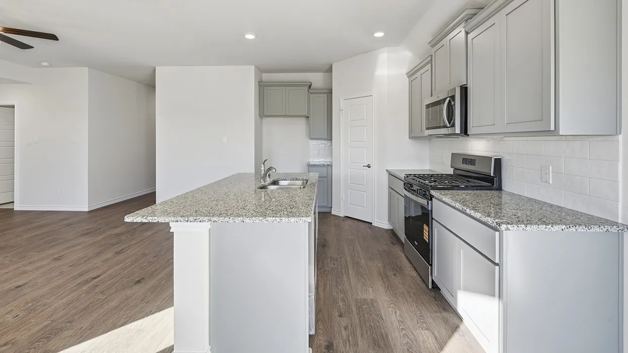 Kitchen featuring light gray cabinetry, stainless steel appliances, speckled countertops, and a subway tile backsplash