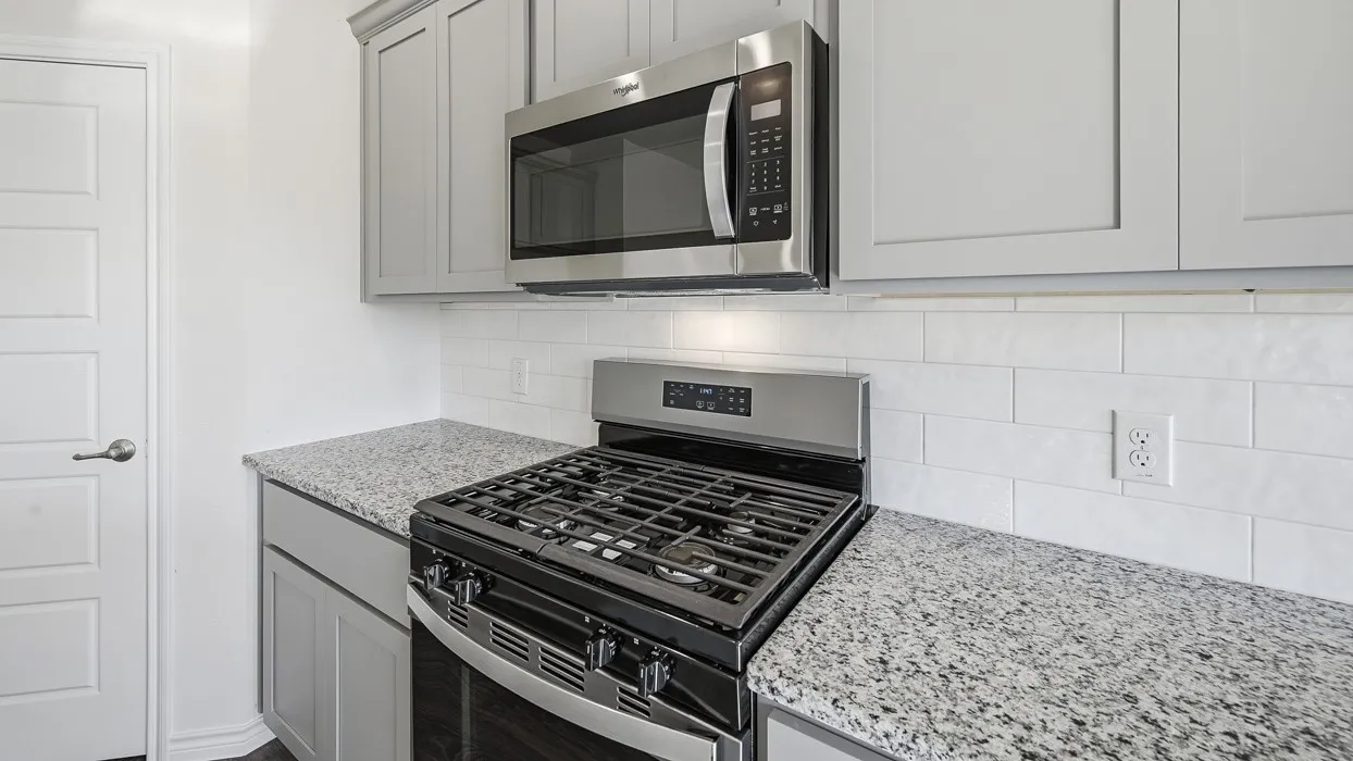 Kitchen featuring light grey cabinetry, a stainless steel gas range, an over-the-range microwave, granite countertops, and a white subway tile backsplash