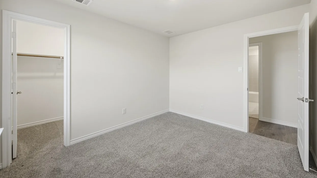 Neutral-toned room featuring light gray carpeting, white baseboards, and a white ceiling with a visible air vent
