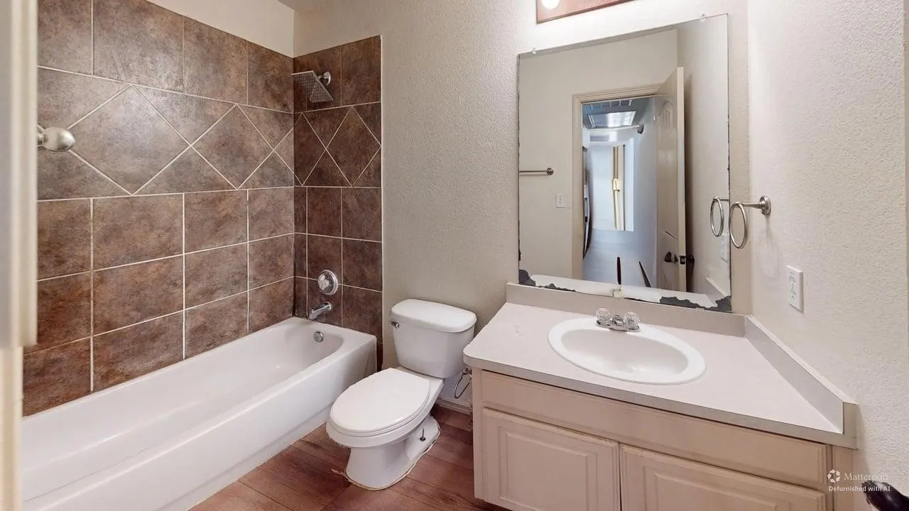 Bathroom featuring a white bathtub, brown tiled shower surround, light-toned vanity with an integrated sink, and wood-finish flooring