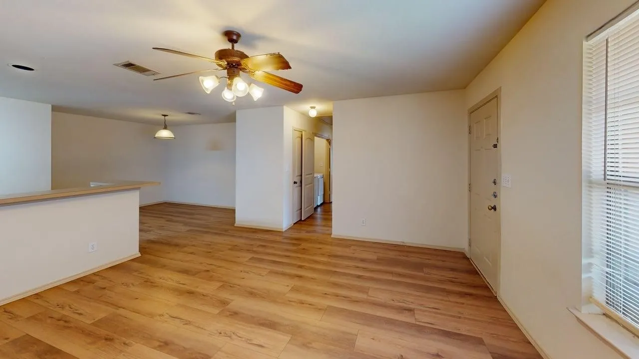 Open-concept living area featuring wood-finish flooring, a ceiling fan with light kit, and neutral wall tones