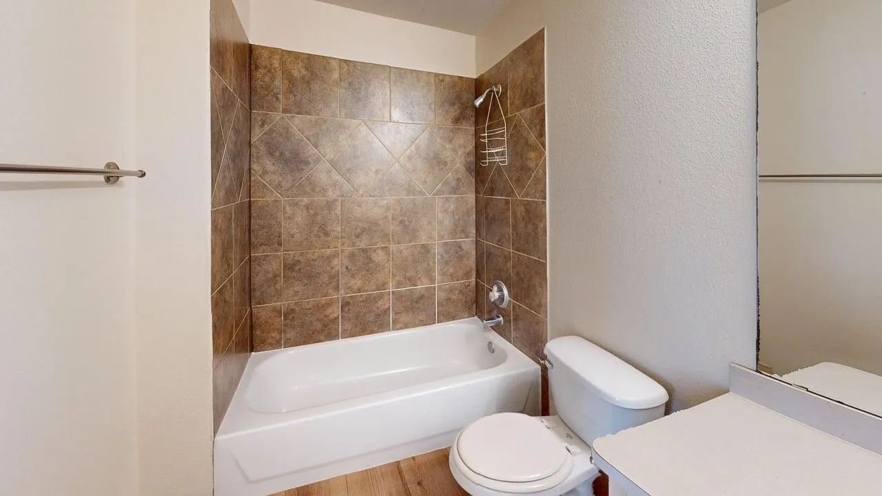 Bathroom featuring a white bathtub, brown tiled shower surround, chrome shower fixtures, and wood-finish flooring