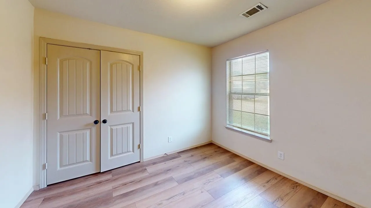 Room featuring wood-finish flooring, light-toned walls, a single-pane window with blinds, and a double-door closet with black hardware