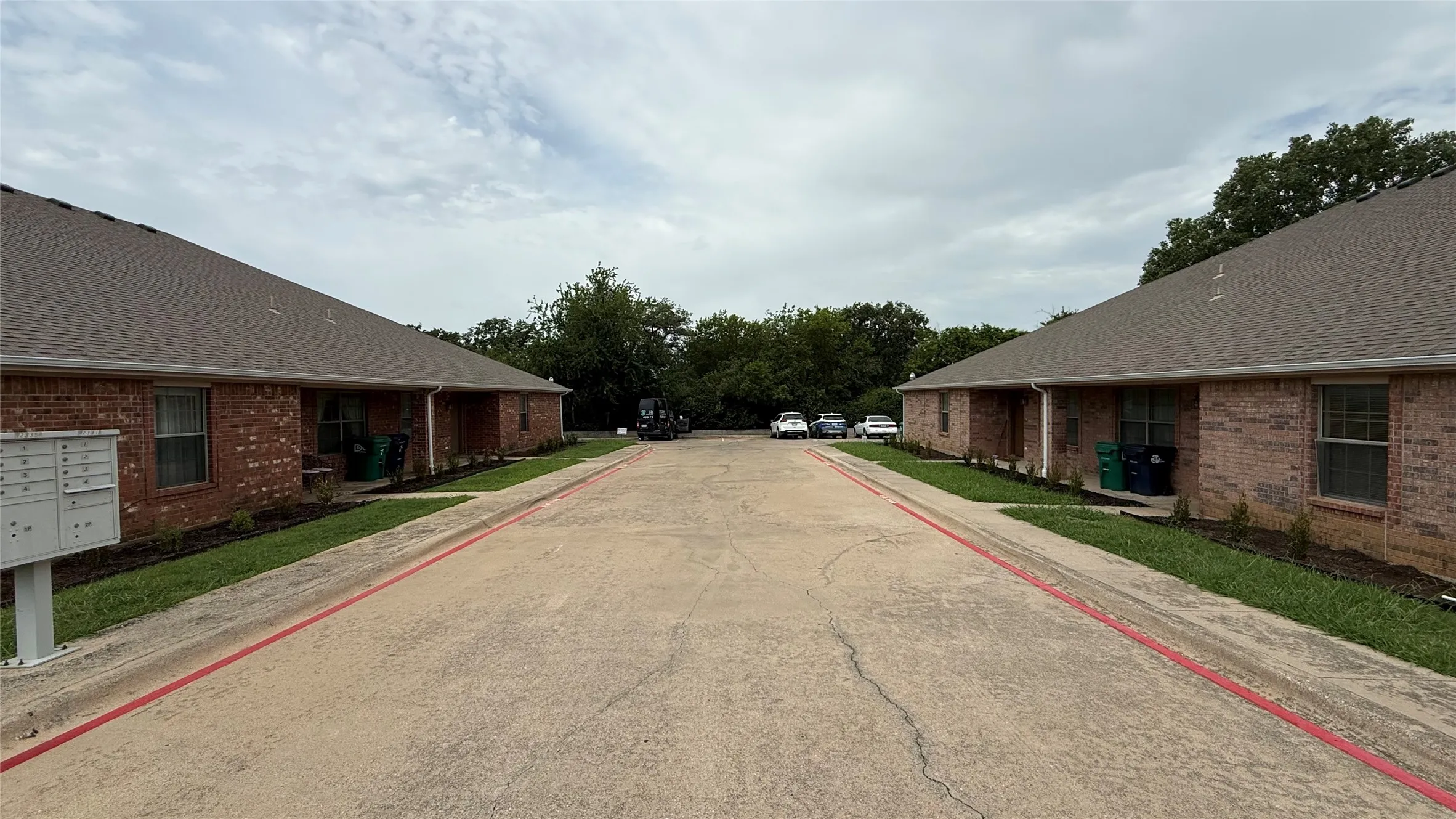 Driveway access with marked fire lanes, flanked by two multi-unit buildings featuring brick exteriors, shingle roofs, and individual entry doors