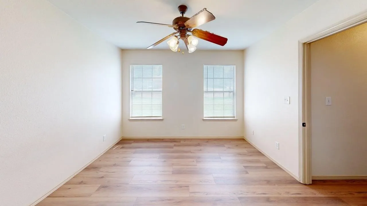 Room featuring wood-finish flooring, two windows with gridded panes, a ceiling fan with integrated lighting, and neutral wall tones