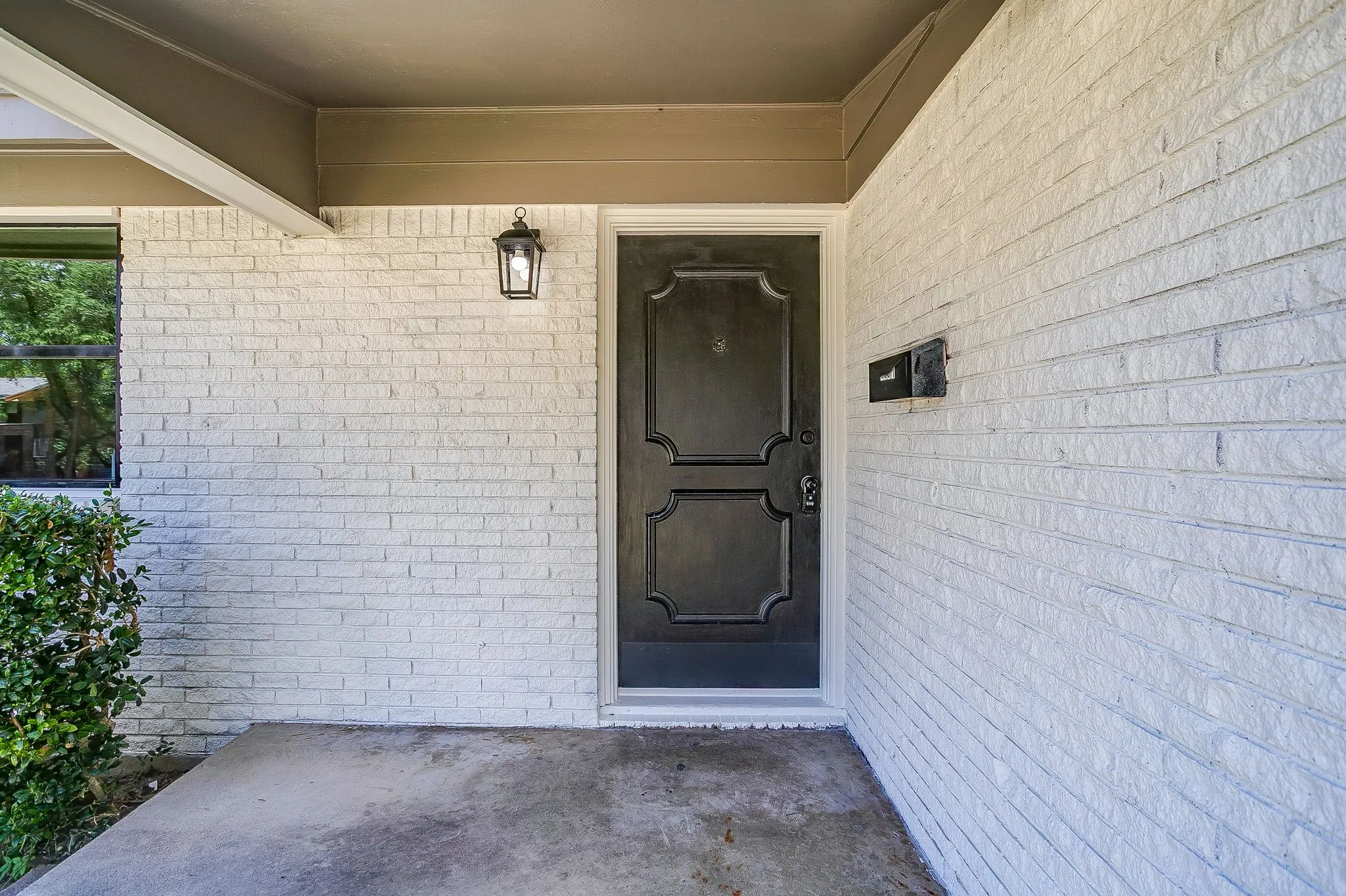 Painted brick exterior with a black panel door, covered entry, black exterior light fixture, and an integrated mailbox