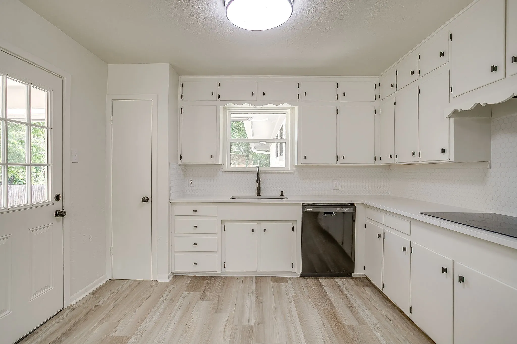 Kitchen featuring white cabinetry, light countertops, wood-finish flooring, a stainless steel dishwasher, and a black cooktop