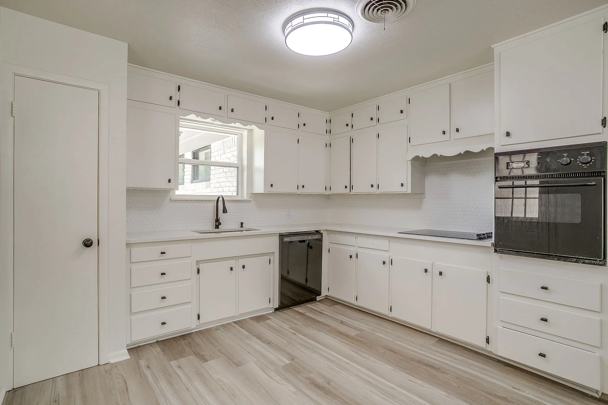 Kitchen featuring white cabinetry, wood-finish flooring, built-in oven, and a black sink with a matching faucet